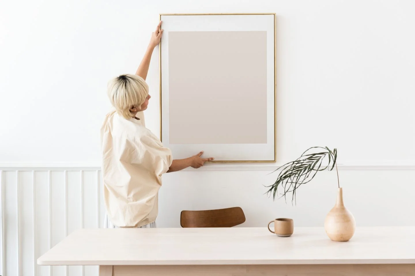 woman hanging a photo frame on a white wall mockup